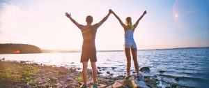 Photo of young sporty couple standing on the coastline with raised arms